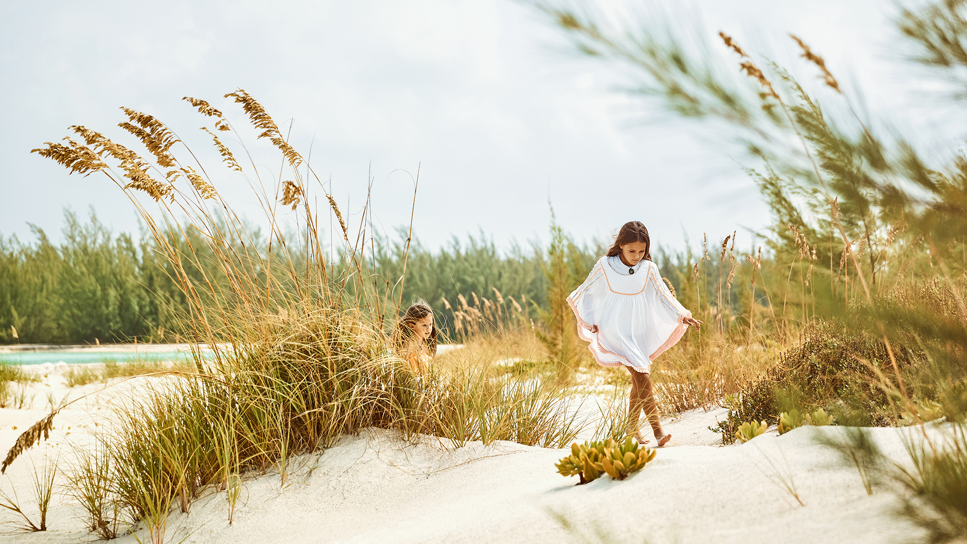 two girls walking on sand in tall grass