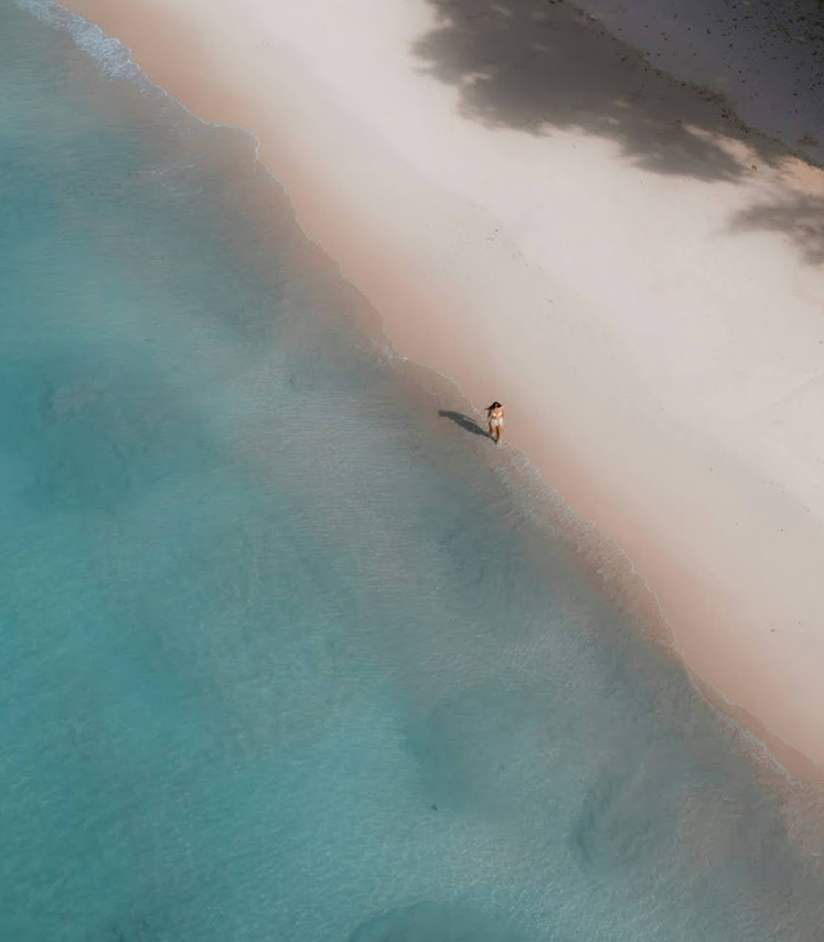 an aerial view of person walking on a secluded beach