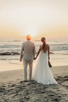 a man in a suit and woman in a wedding dress holding hands on a beach