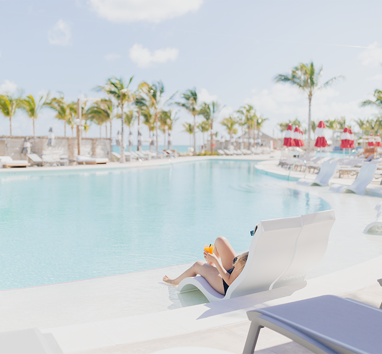 a woman sitting on a lounge chair by a pool