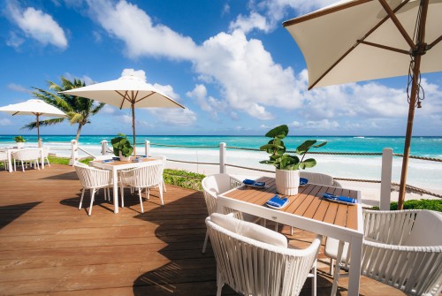 a table and chairs on a deck with a beach and ocean in the background