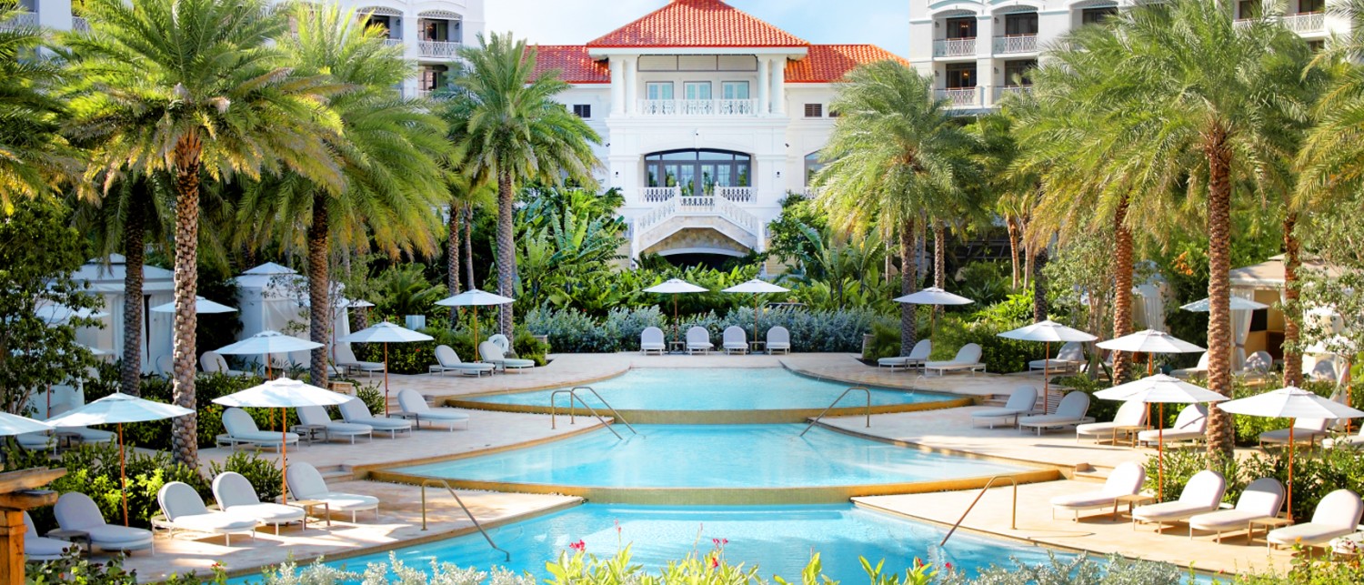 a pool with palm trees and umbrellas and Rosewood Baha Mar resort