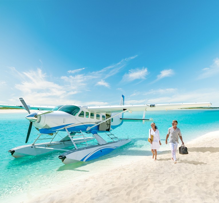 a man and woman walking on a beach with a seaplane in the water