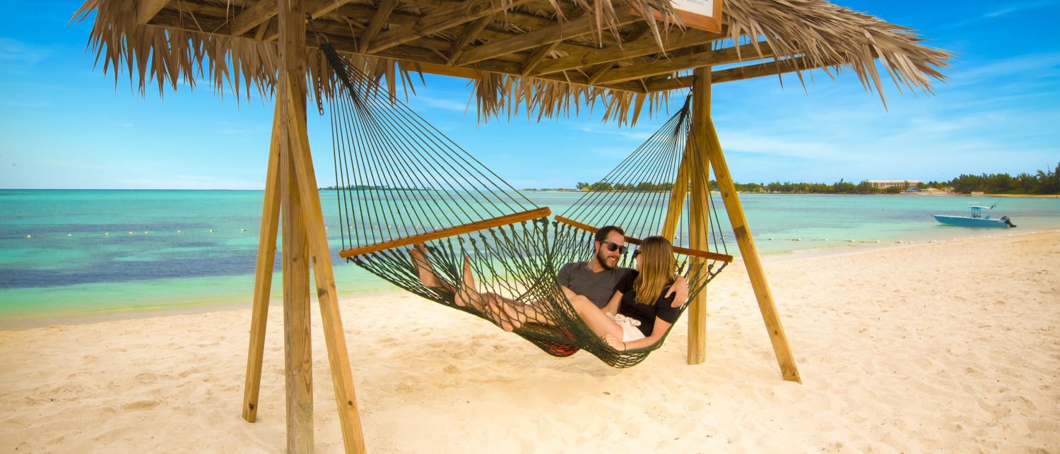 a man and woman lying in a hammock on a beach
