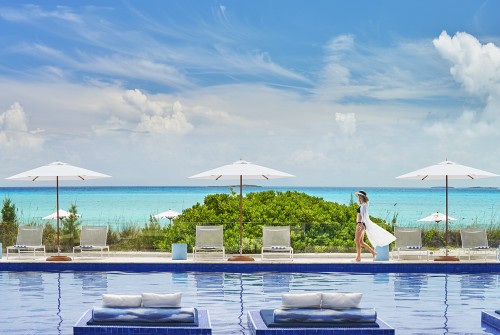 a woman walking by a pool with umbrellas and chairs