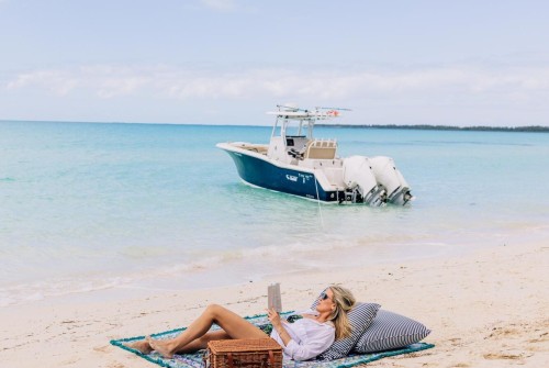 a woman lying on a blanket on a beach with a boat in the background