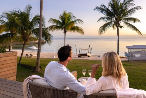 a man and woman sitting on a deck with palm trees and a body of water