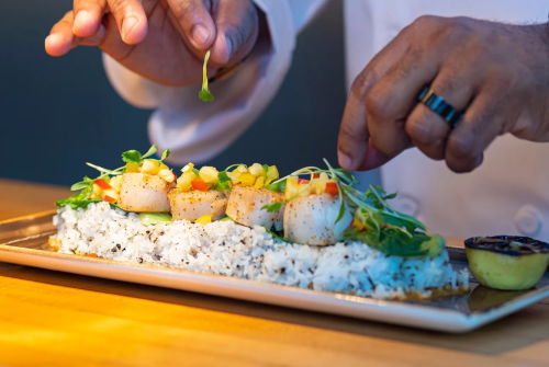 a person's hands sprinkling a leaf on a plate of food