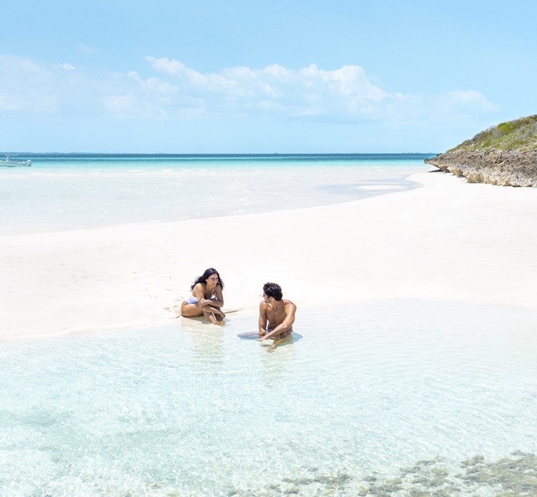 a man and woman sitting in water on a beach