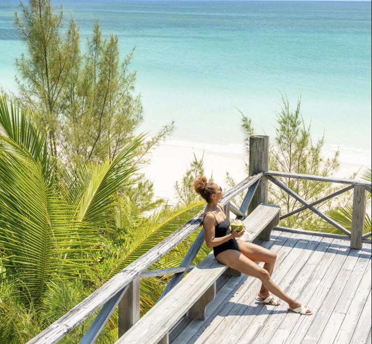 a woman sitting on a wooden deck overlooking a beach