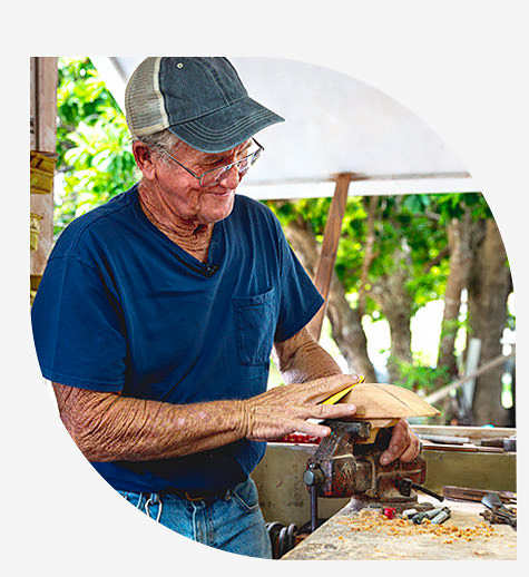 top image man with blue shirt carving wood bottom image ocean with board walk 